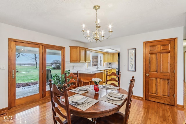 dining area featuring an inviting chandelier, sink, a healthy amount of sunlight, and light wood-type flooring