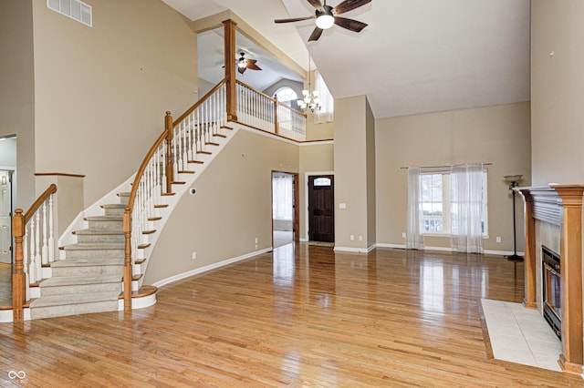 unfurnished living room featuring a towering ceiling, a fireplace, light hardwood / wood-style floors, and ceiling fan with notable chandelier