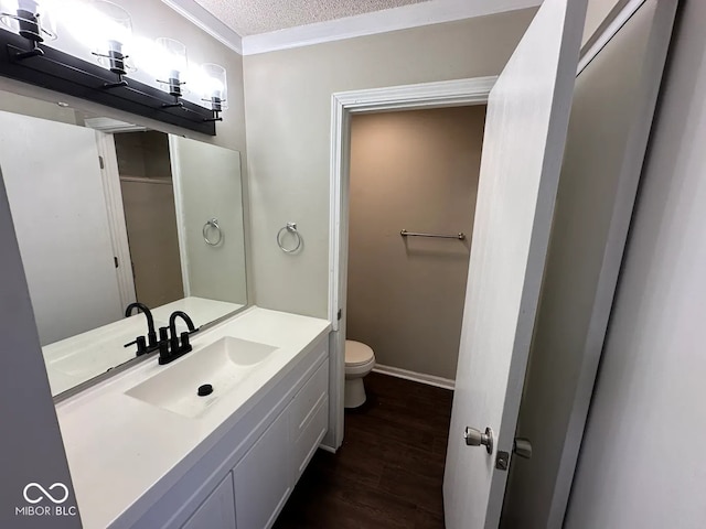 bathroom with hardwood / wood-style flooring, vanity, ornamental molding, toilet, and a textured ceiling