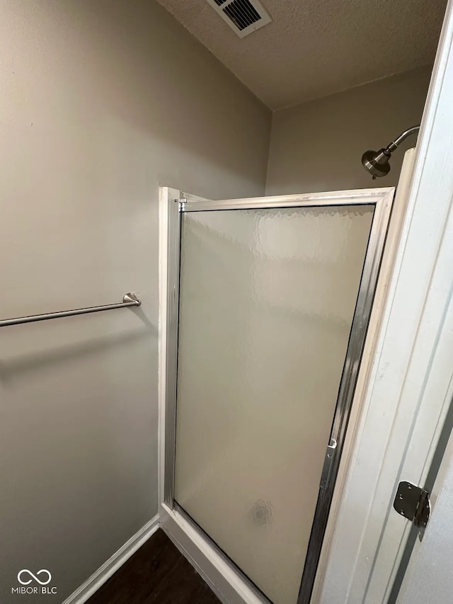 bathroom with hardwood / wood-style flooring, a shower with door, and a textured ceiling