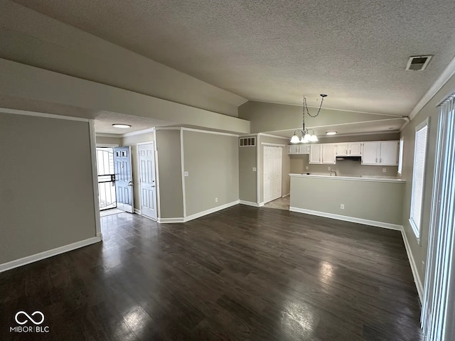 unfurnished living room featuring dark wood-type flooring, lofted ceiling, a textured ceiling, ornamental molding, and a notable chandelier