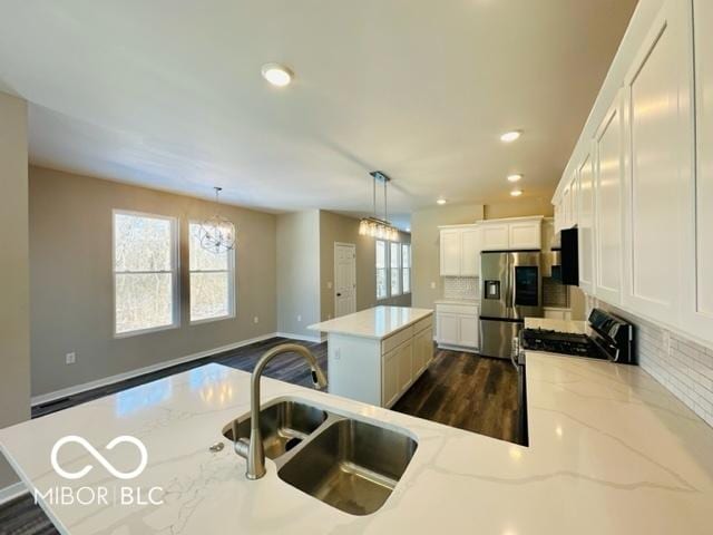 kitchen with stainless steel refrigerator with ice dispenser, sink, light stone counters, a kitchen island, and pendant lighting