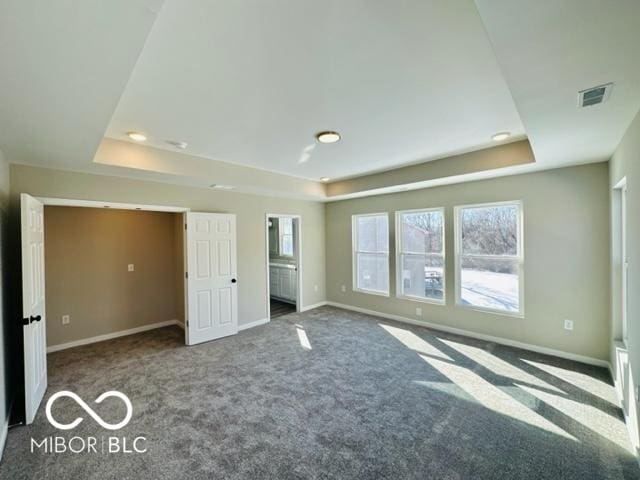 unfurnished bedroom with a tray ceiling and dark colored carpet