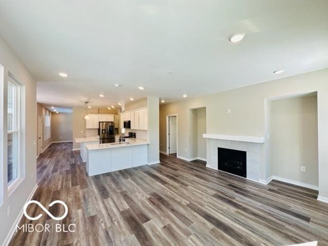 kitchen with dark hardwood / wood-style floors, white cabinets, a tiled fireplace, kitchen peninsula, and stainless steel refrigerator with ice dispenser