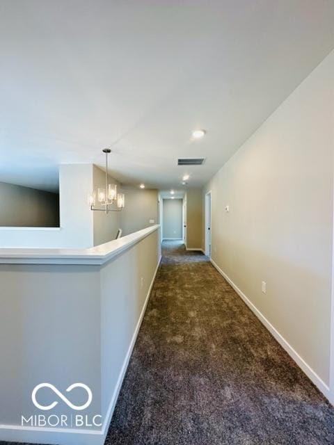 hallway with a chandelier and dark carpet