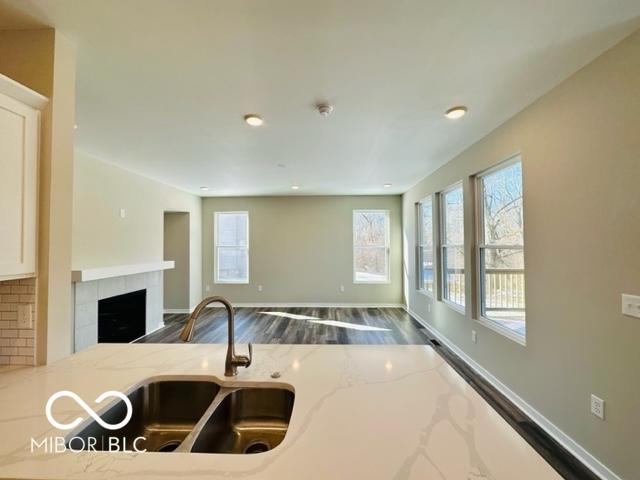 kitchen with wood-type flooring, sink, decorative backsplash, a tiled fireplace, and light stone countertops