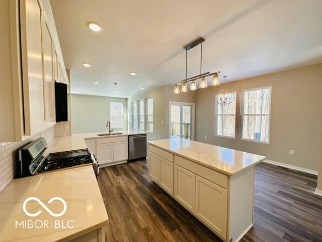 kitchen with appliances with stainless steel finishes, hanging light fixtures, a center island, light stone countertops, and dark hardwood / wood-style flooring