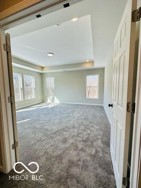 unfurnished room with a healthy amount of sunlight, a raised ceiling, and dark colored carpet