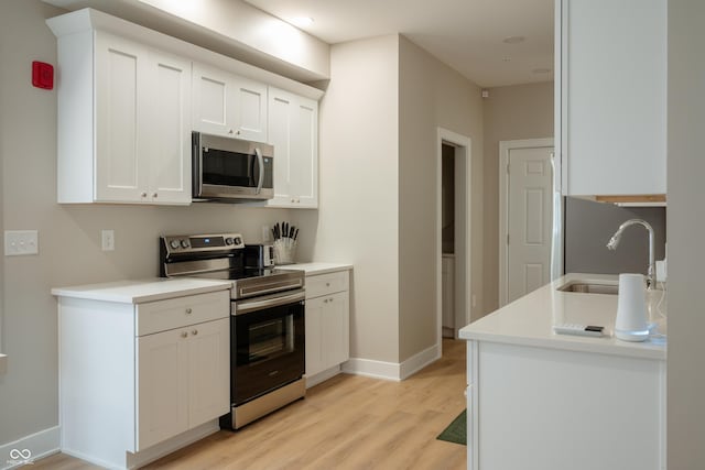 kitchen with light wood-type flooring, stainless steel appliances, sink, and white cabinets