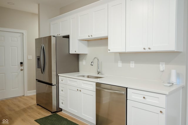 kitchen with appliances with stainless steel finishes, sink, white cabinets, and light hardwood / wood-style floors