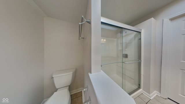 bathroom with tile patterned flooring, toilet, and a shower with shower door