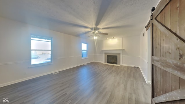 unfurnished living room featuring light hardwood / wood-style flooring, ceiling fan, a fireplace, a textured ceiling, and a barn door