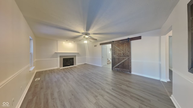 unfurnished living room with ceiling fan, a barn door, and hardwood / wood-style floors