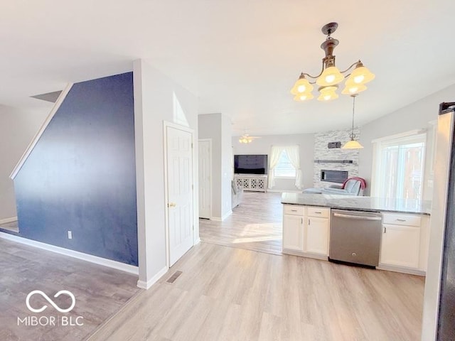 kitchen featuring appliances with stainless steel finishes, a stone fireplace, pendant lighting, white cabinets, and light hardwood / wood-style floors