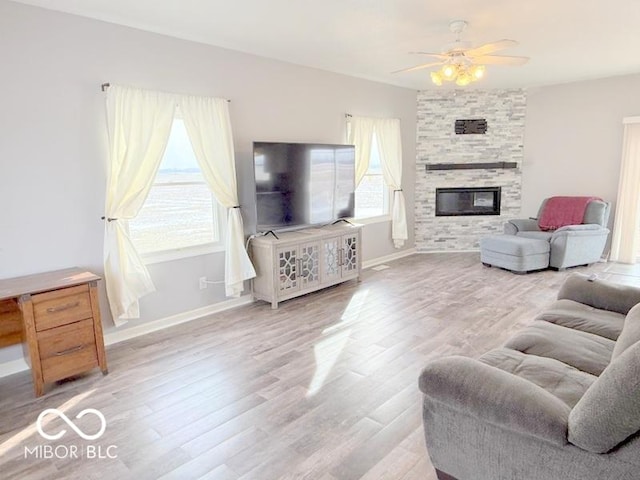 living room featuring hardwood / wood-style flooring, ceiling fan, a healthy amount of sunlight, and a stone fireplace