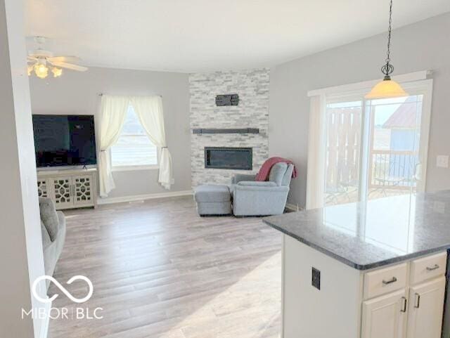 interior space featuring a stone fireplace, light hardwood / wood-style floors, white cabinets, decorative light fixtures, and dark stone counters