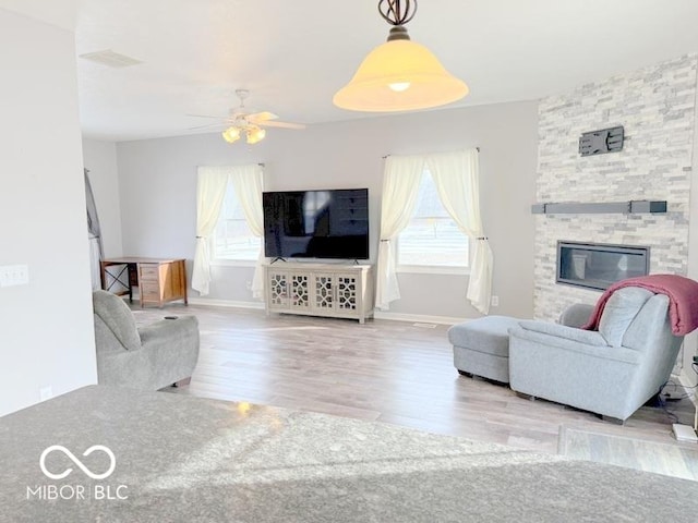 living room featuring ceiling fan, a fireplace, and light hardwood / wood-style floors