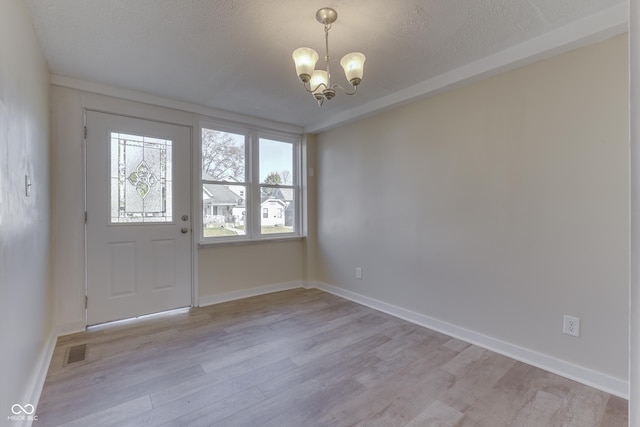 unfurnished room featuring an inviting chandelier, a textured ceiling, and light wood-type flooring