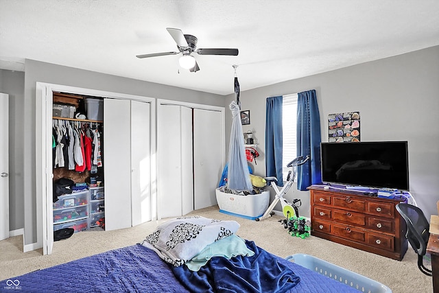 carpeted bedroom with two closets, a textured ceiling, and ceiling fan