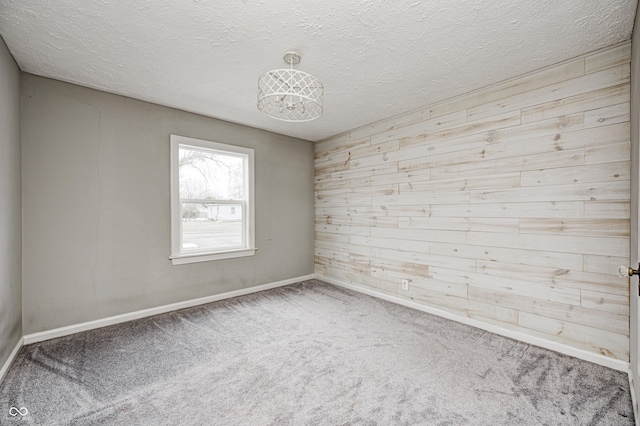 spare room featuring carpet flooring, a textured ceiling, and wood walls