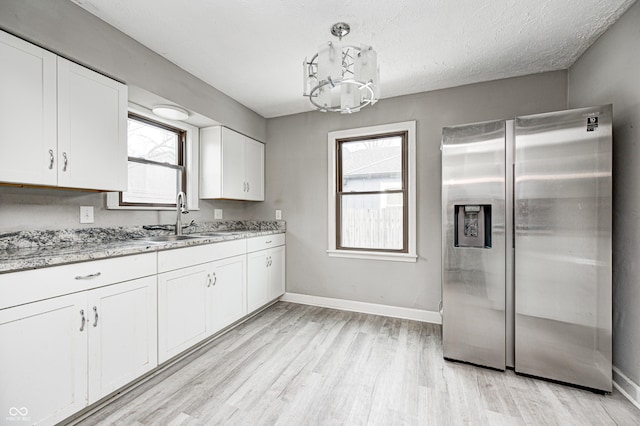 kitchen featuring light stone counters, stainless steel fridge, sink, and white cabinets