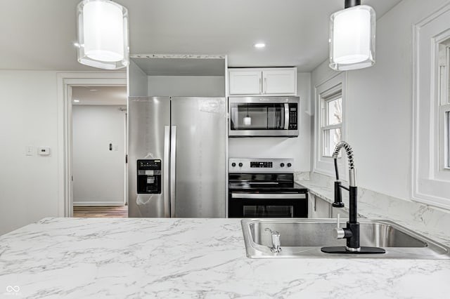 kitchen with sink, white cabinetry, hanging light fixtures, stainless steel appliances, and light stone counters