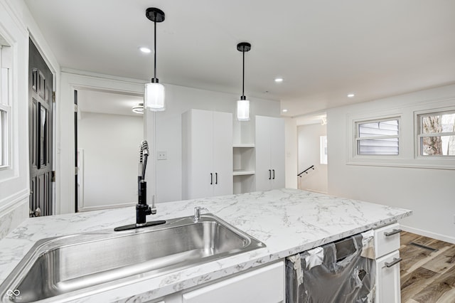 kitchen with sink, stainless steel dishwasher, pendant lighting, light hardwood / wood-style floors, and white cabinets