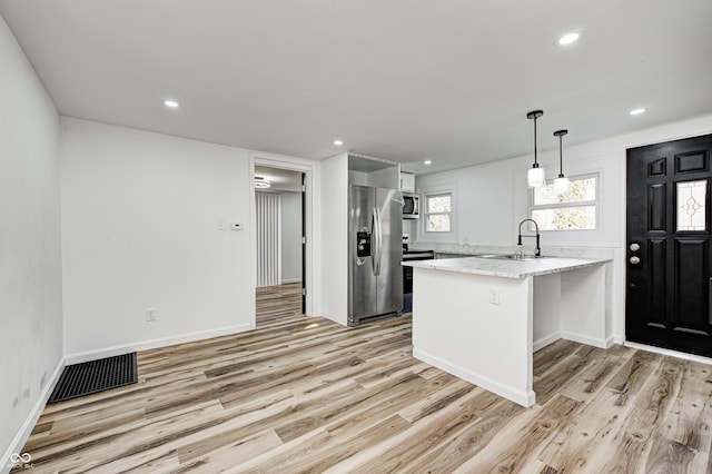 kitchen with appliances with stainless steel finishes, decorative light fixtures, sink, kitchen peninsula, and light hardwood / wood-style flooring