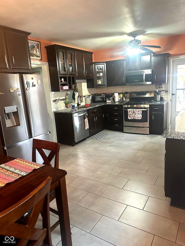 kitchen with tasteful backsplash, dark brown cabinets, appliances with stainless steel finishes, ceiling fan, and light stone countertops