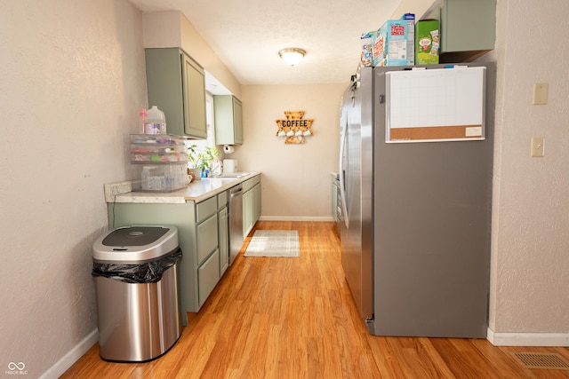 kitchen with stainless steel appliances, green cabinets, and light wood-type flooring