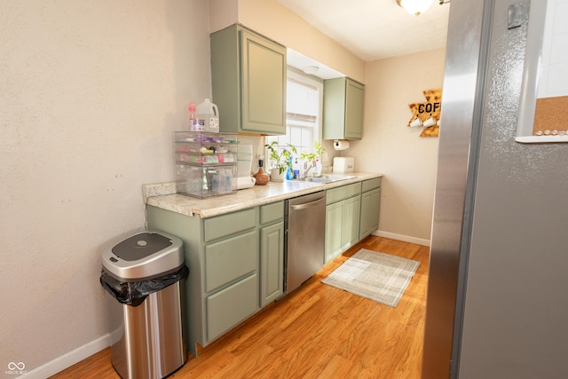 kitchen featuring sink, stainless steel dishwasher, light wood-type flooring, and green cabinetry