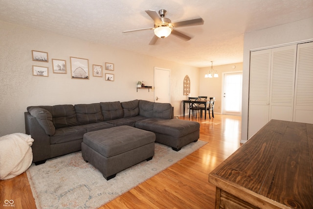 living room with ceiling fan with notable chandelier, light hardwood / wood-style floors, and a textured ceiling