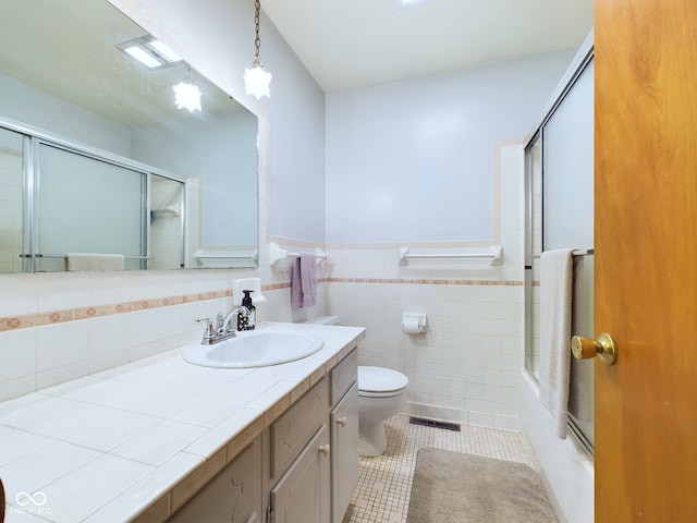 full bathroom with tile walls, shower / bath combination with glass door, vanity, toilet, and tile patterned floors