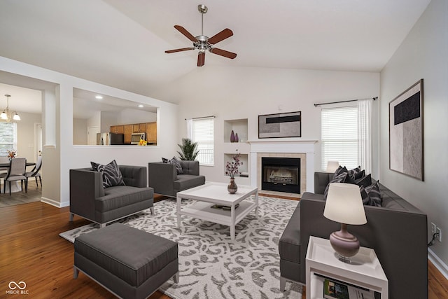 living room featuring a fireplace, lofted ceiling, wood finished floors, baseboards, and ceiling fan with notable chandelier