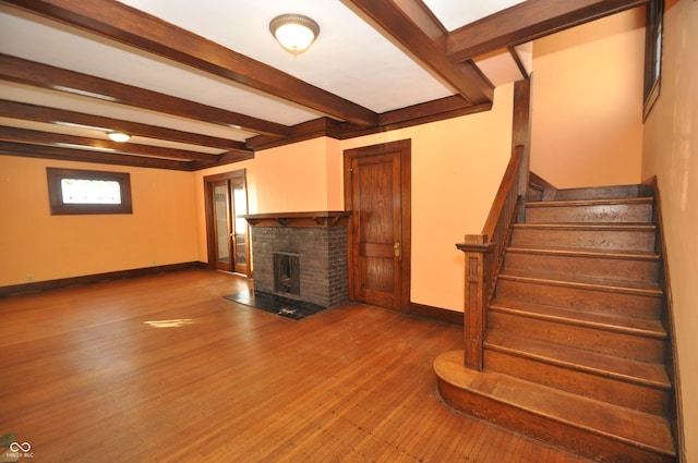 unfurnished living room featuring beamed ceiling, hardwood / wood-style floors, and a brick fireplace