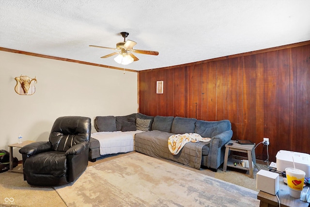 living room featuring wood walls, crown molding, light carpet, a textured ceiling, and ceiling fan