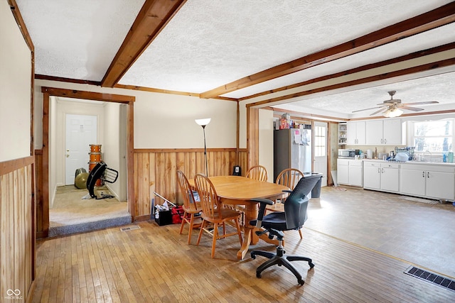 dining room with beamed ceiling, sink, ceiling fan, light hardwood / wood-style floors, and a textured ceiling