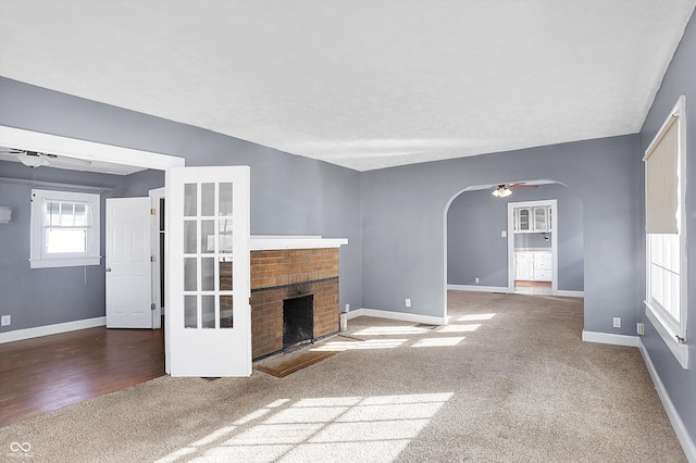 unfurnished living room featuring ceiling fan, dark carpet, and a brick fireplace