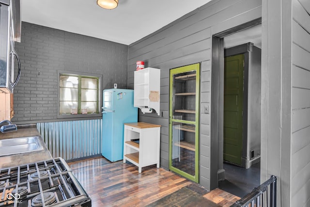 kitchen featuring wooden walls, refrigerator, sink, dark wood-type flooring, and gas range oven