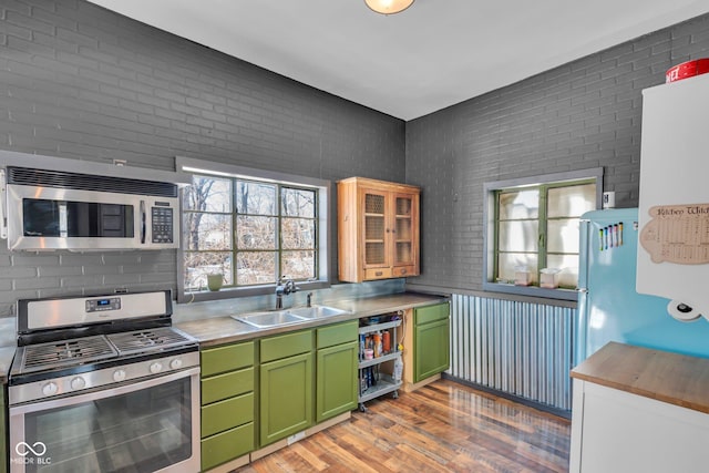 kitchen with stainless steel appliances, brick wall, sink, and green cabinets