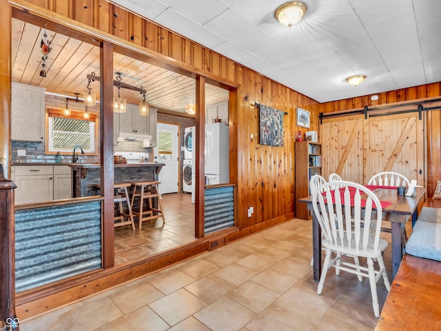 dining area featuring wooden walls, sink, a barn door, and stacked washing maching and dryer