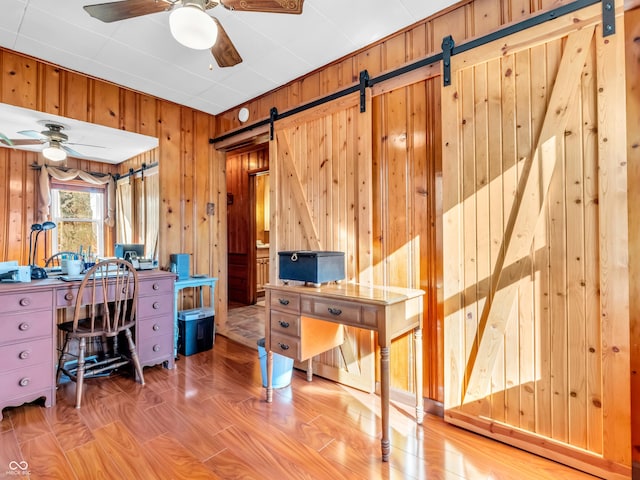 home office with ceiling fan, a barn door, and wood walls