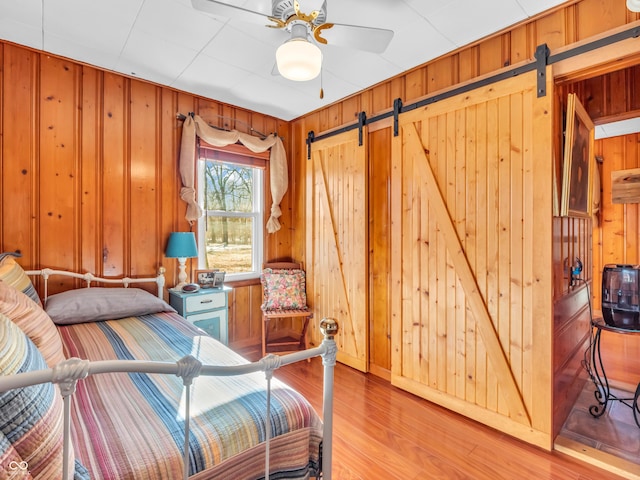 bedroom with wooden walls, ceiling fan, a barn door, and light hardwood / wood-style flooring