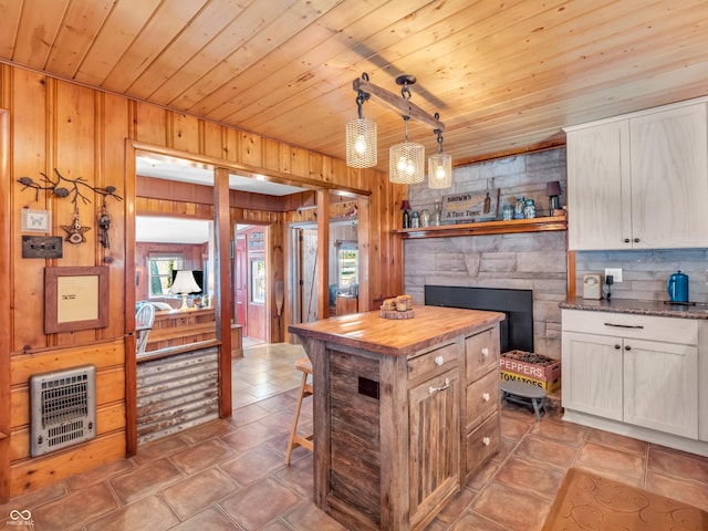 kitchen with white cabinetry, decorative light fixtures, heating unit, and wood walls