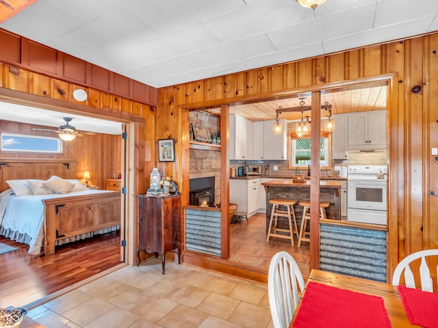 interior space featuring hanging light fixtures, white range with electric stovetop, white cabinets, light tile patterned flooring, and decorative backsplash