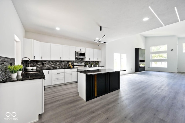 kitchen featuring a kitchen island, appliances with stainless steel finishes, high vaulted ceiling, white cabinets, and hanging light fixtures