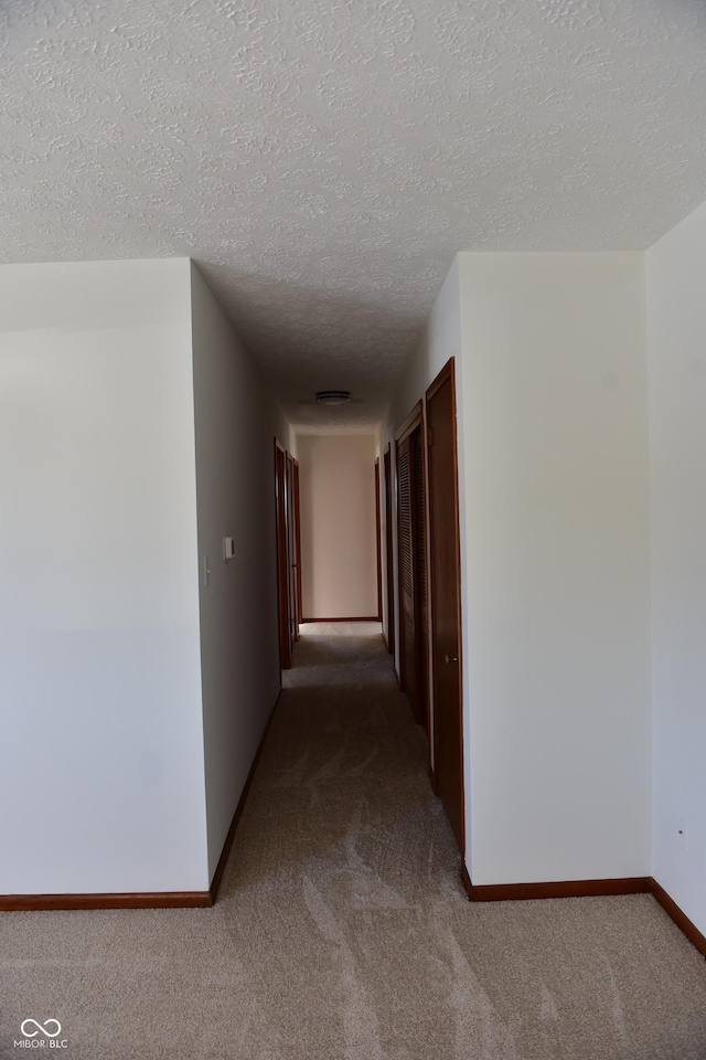 corridor with a textured ceiling and carpet flooring