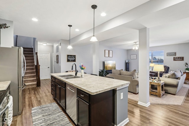 kitchen with sink, hardwood / wood-style floors, hanging light fixtures, stainless steel appliances, and a center island with sink