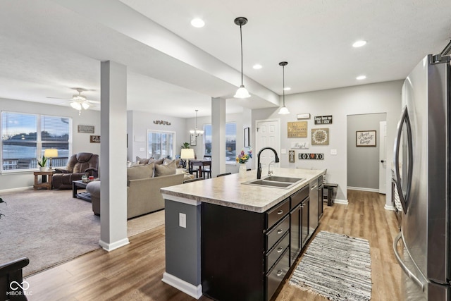 kitchen with stainless steel refrigerator, decorative light fixtures, sink, hardwood / wood-style flooring, and a center island with sink