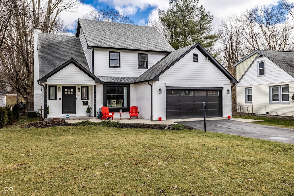 view of front of home with driveway, brick siding, a shingled roof, an attached garage, and a front yard